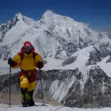 Alix von Melle, in voller Bergsteigerausrüstung, steht auf einem schneebedeckten Gipfel vor einer majestätischen Bergkulisse.