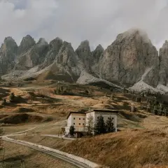 Majestätische Berge im Val di Funes, ein Hotel auf einem Hügel, umgeben von herbstlichem Gras und einer Straße.
