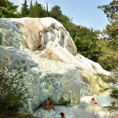 Natürliche Kalkformationen und türkisfarbene Thermalbecken in Bagni San Filippo. Menschen entspannen sich im warmen Wasser.