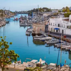 Hafen von Ciutadella, Menorca. Boote im türkisfarbenen Wasser, weiße Häuser und bunte Fassaden. Ein malerischer Blick auf die Menorca Highlights.