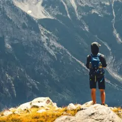 Ein Wanderer mit Rucksack steht auf einem Felsen und blickt in die majestätische Berglandschaft Albaniens.