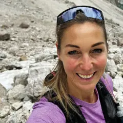 Eva Sperger lächelt in die Kamera, während sie auf einem steinigen Bergpfad unterwegs ist.