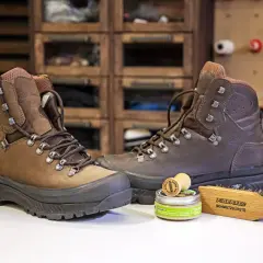 Zwei braune Wanderschuhe bereit zum Reinigen, daneben eine Dose Wachs und eine Bürste.