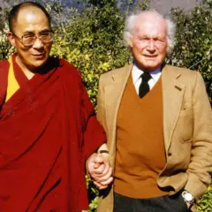 Der Dalai Lama und Heinrich Harrer, ein Freund Tibets, halten Händchen vor üppigem Grün.
