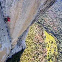 Ein Kletterer bezwingt eine riesige Felswand im Stil des free solo film. Tief unten schlängelt sich ein Fluss durch einen grünen Wald.