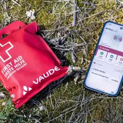Erste Hilfe Set und Smartphone mit Notruf-App liegen im Gras. Wichtig für die Sicherheit beim Wandern.