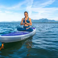 Frau praktiziert SUP Yoga auf einem Brett im See, mit Bergen im Hintergrund.