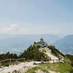 Auf einer Kehlsteinhaus Wanderung genießt man diese Aussicht: Ein Haus thront auf einem Berg, umgeben von grünen Wäldern und majestätischen Alpen.