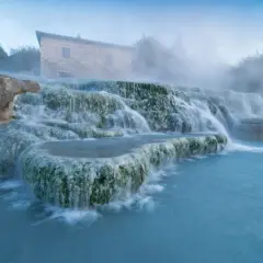 Toskana: malerische schwefelquellen mit einem alten Steinhaus im Hintergrund und dampfendem, türkisfarbenem Wasser.