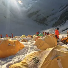 Bergsteiger in orangefarbenen Anzügen bereiten sich auf den Aufstieg vom Mount Everest Camp 4 vor. Gelbe Zelte sind im Schnee verstreut.