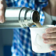 Eine Person gießt Kaffee aus einer Thermoskanne in eine Tasse. Die Thermoskanne reinigen ist wichtig für den Geschmack.