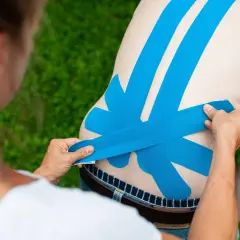 Eine Person legt blaues Tape auf den Rücken eines Mannes. Das Tape dient als Unterstützung und zur Linderung von Schmerzen.