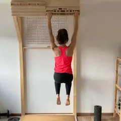 Frau hängt an einem Hangboard für intensives **Hangboard Training**. Trainingsplan hängt an der Wand.