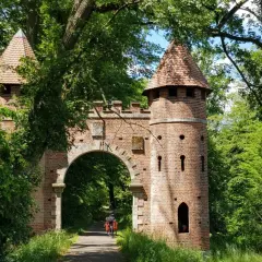Ein Torbogen mit Türmen, umgeben von üppigem Grün. Ein Radfahrer fährt hindurch. Ein echter Geheimtipp in Wittenberg für Naturliebhaber.