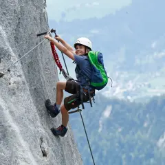 Ein Junge mit Helm und Rucksack klettert einen Felsgrat. Ein spannendes Abenteuer für klettersteig kinder.
