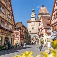 Fachwerkhäuser säumen die Gasse in Rothenburg ob der Tauber. Ein Uhrenturm überragt die Szene, während Touristen die mittelalterliche Stadt erkunden.