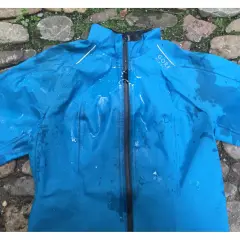 Blaue Gore-Tex Regenjacke mit Wasserflecken, bereit zum Trocknen auf einem steinigen Untergrund.