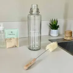 Alles für die Edelstahl Trinkflasche reinigen: Spülmittel, Pulver, Flaschenbürste und ein kleiner Topf mit Pflanze.