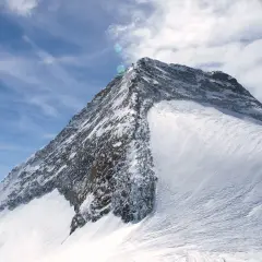 Der majestätische Olperer Nordgrat, bedeckt mit glitzerndem Schnee, ragt unter einem strahlend blauen Himmel mit zarten Wolken empor.