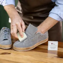 Mann reinigt graue Nubukleder-Sneaker mit einem speziellen Radierer. Die richtige nubukleder pflege erhält die Schuhe.
