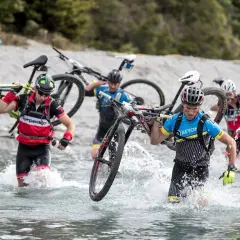 Teilnehmer eines **adventure racing** durchqueren mit ihren Mountainbikes einen Fluss.