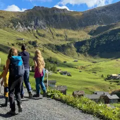 Familie genießt das Liechtenstein wandern in den Alpen. Grüne Hänge, kleine Häuser und ein Bergpanorama.