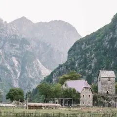 Steinerne Häuser und ein alter Turm in Albanien Theth, umgeben von majestätischen, nebelverhangenen Bergen.