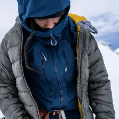 Person in Daunenjacke im Schnee. Die Jacke ist grau, darunter eine blaue Schicht. Perfekt für das Daunenjacke waschen nach einer Bergtour.