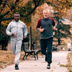Zwei Männer im Herbstpark trainieren für den Halbmarathon. Sie laufen auf einem Weg, umgeben von bunten Blättern.