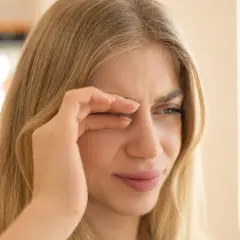 Junge Frau reibt sich die Augen, weil sie flimmern vor den Augen hat. Wahrscheinlich hat sie zu wenig getrunken.