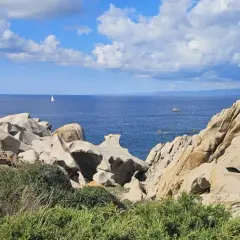 Felsformationen am Capo Testa, Sardinien, mit Blick auf das blaue Meer und eine einsame Segelyacht.