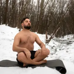 Mann in der Natur, barbusig im Schnee sitzend, praktiziert Wim Hof Atmung.