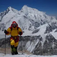 Alix von Melle, in voller Bergsteigerausrüstung, steht auf einem schneebedeckten Gipfel vor einer majestätischen Bergkulisse.