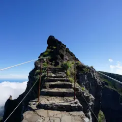 Steile Steintreppe, die sich den Berg hinaufwindet, mit Seilen gesichert. Eine Himmelsleiter auf Madeira, die über den Wolken in den blauen Himmel führt.