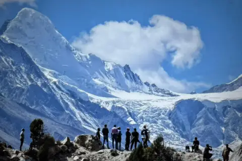 Bergsteiger bestaunen die majestätische Rupal-Wand, einen eisigen Riesen unter blauem Himmel.