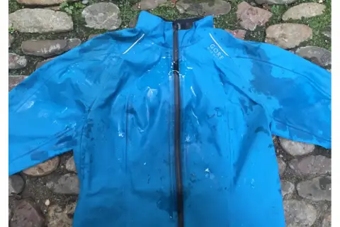 Blaue Gore-Tex Regenjacke mit Wasserflecken, bereit zum Trocknen auf einem steinigen Untergrund.