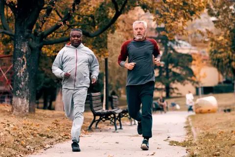 Zwei Männer im Herbstpark trainieren für den Halbmarathon. Sie laufen auf einem Weg, umgeben von bunten Blättern.