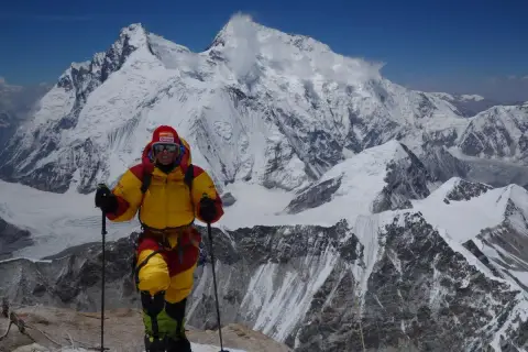 Alix von Melle, in voller Bergsteigerausrüstung, steht auf einem schneebedeckten Gipfel vor einer majestätischen Bergkulisse.