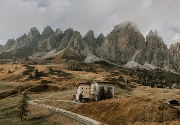 Majestätische Berge im Val di Funes, ein Hotel auf einem Hügel, umgeben von herbstlichem Gras und einer Straße.