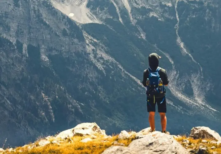 Ein Wanderer mit Rucksack steht auf einem Felsen und blickt in die majestätische Berglandschaft Albaniens.