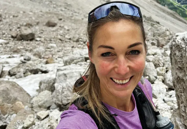 Eva Sperger lächelt in die Kamera, während sie auf einem steinigen Bergpfad unterwegs ist.