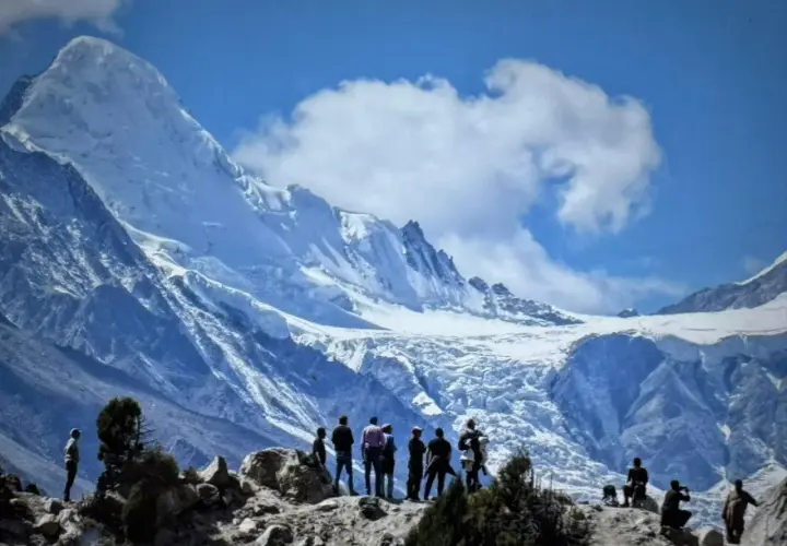 Bergsteiger bestaunen die majestätische Rupal-Wand, einen eisigen Riesen unter blauem Himmel.