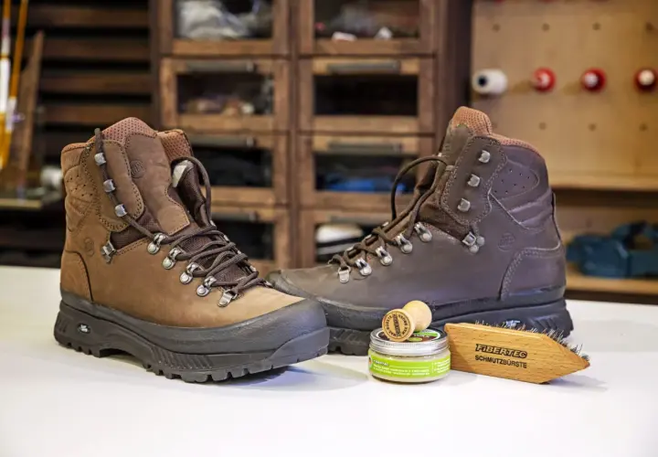 Zwei braune Wanderschuhe bereit zum Reinigen, daneben eine Dose Wachs und eine Bürste.