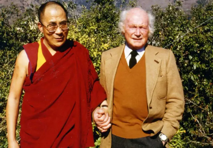 Der Dalai Lama und Heinrich Harrer, ein Freund Tibets, halten Händchen vor üppigem Grün.