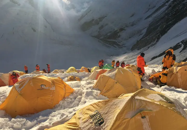 Bergsteiger in orangefarbenen Anzügen bereiten sich auf den Aufstieg vom Mount Everest Camp 4 vor. Gelbe Zelte sind im Schnee verstreut.
