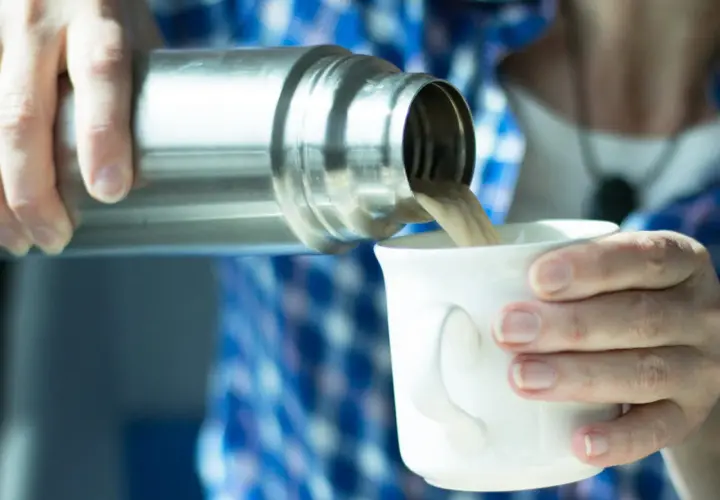 Eine Person gießt Kaffee aus einer Thermoskanne in eine Tasse. Die Thermoskanne reinigen ist wichtig für den Geschmack.