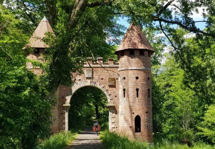 Ein Torbogen mit Türmen, umgeben von üppigem Grün. Ein Radfahrer fährt hindurch. Ein echter Geheimtipp in Wittenberg für Naturliebhaber.