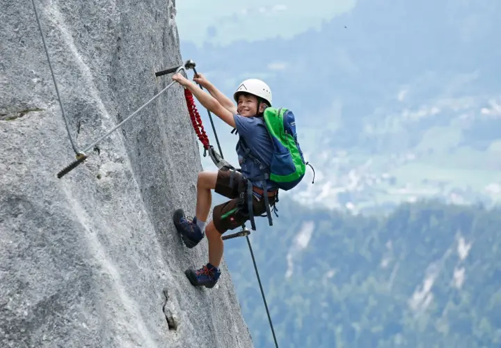 Ein Junge mit Helm und Rucksack klettert einen Felsgrat. Ein spannendes Abenteuer für klettersteig kinder.