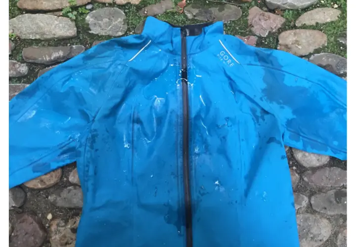 Blaue Gore-Tex Regenjacke mit Wasserflecken, bereit zum Trocknen auf einem steinigen Untergrund.