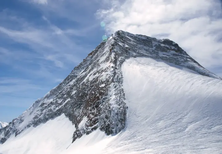 Der majestätische Olperer Nordgrat, bedeckt mit glitzerndem Schnee, ragt unter einem strahlend blauen Himmel mit zarten Wolken empor.